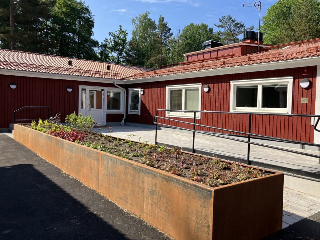 Entrén på Sundshagen Nedre – ett rött hus med vita knutar med ramp och räcke för tillgänglighetsanpassning.