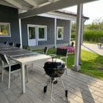 Terass utomhus med grill och långbord för måltider