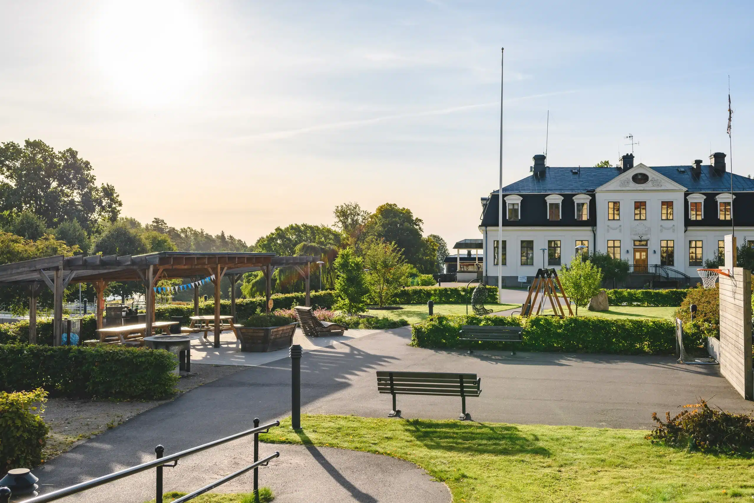 Aktivitetspark med grillplats, bänkar och lekredskap framför den vita herrgården Vitahuset.