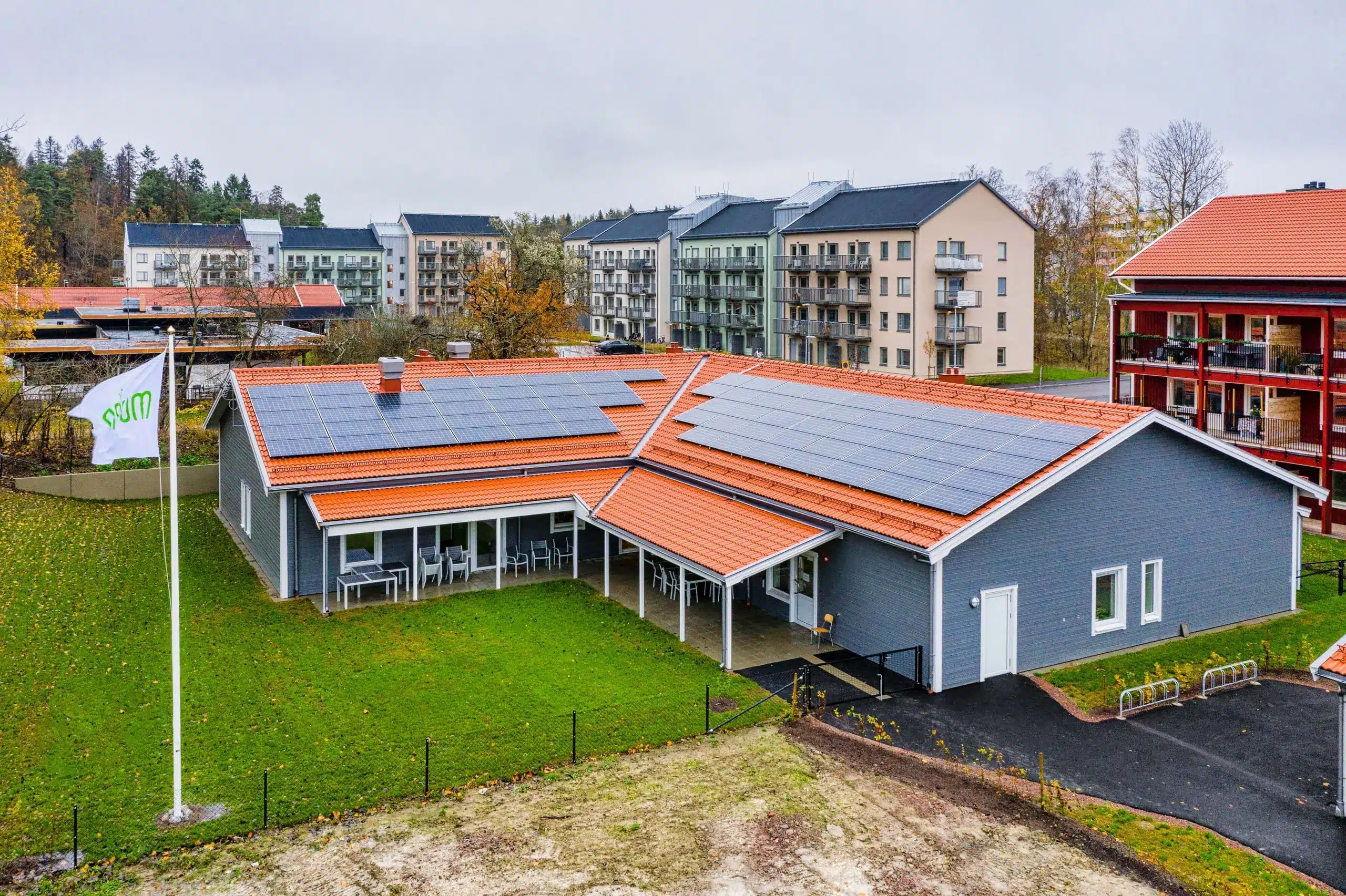 Flygbild över ett låghus med solpaneler och orange tegeltak, omgivet av flerbostadshus i Nyköping.